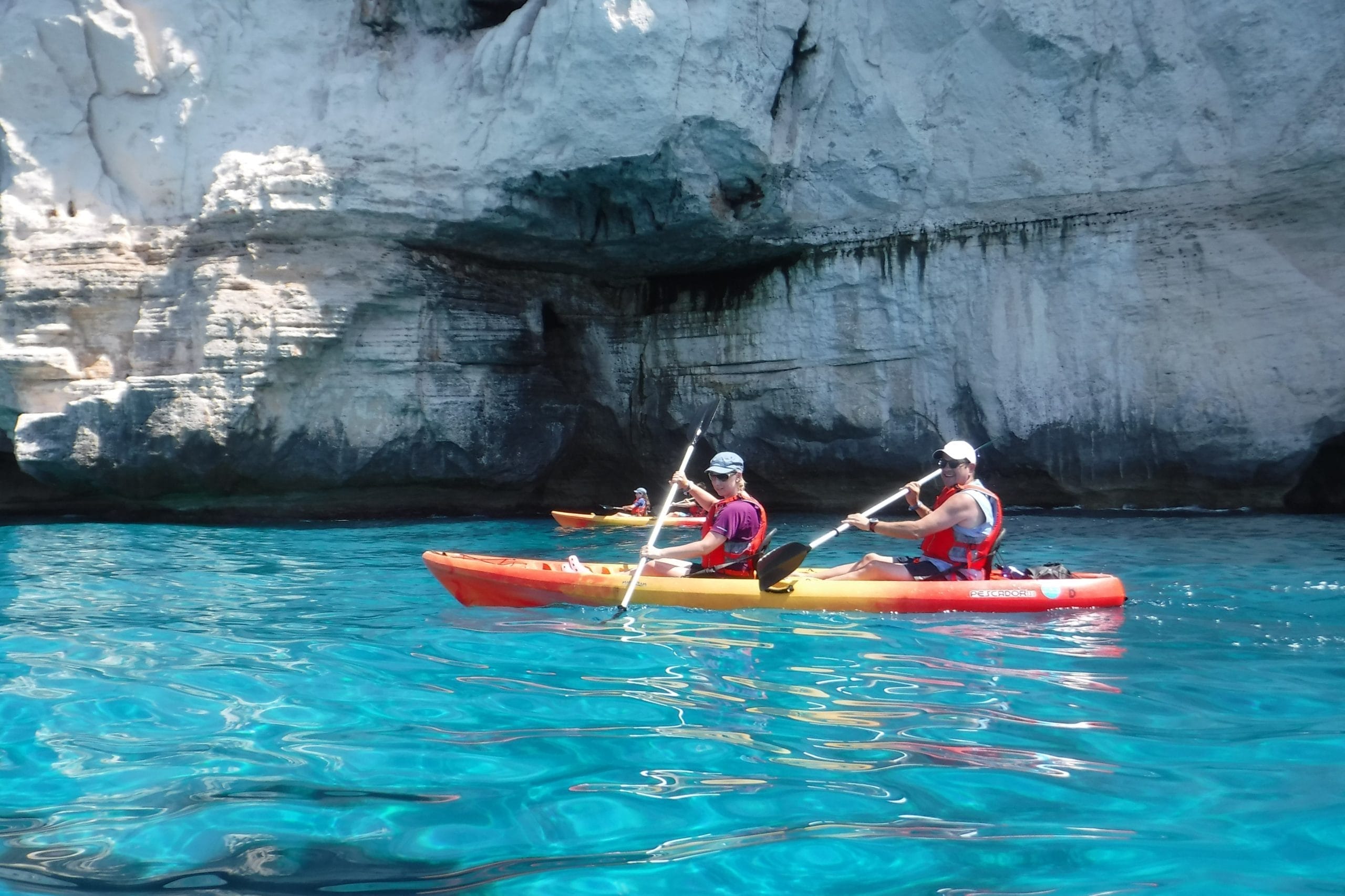 Kayak navegando por aguas cristalinas en una zona de acantilados y cuevas en el sur de Menorca