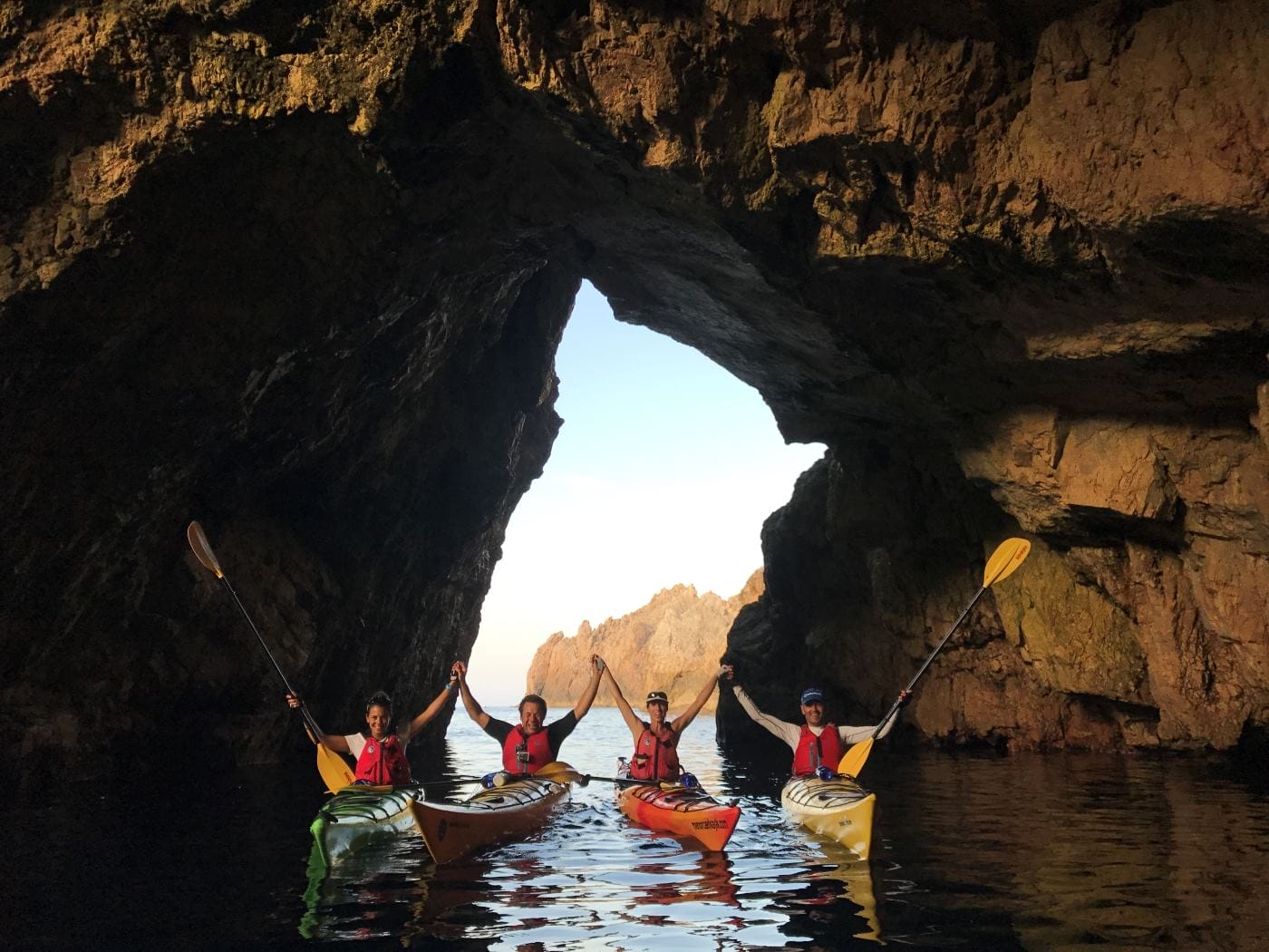 Explorando una cueva marina en kayak de mar durante nuestra ruta de 4 días por Menorca. Los 4 kayakistas tienen las palas levantadas con entusiasmo.