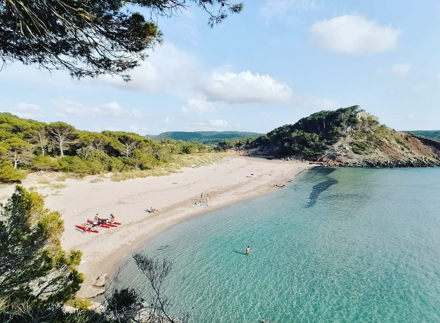 Vista aérea de una playa paradisíaca en Menorca, con kayaks rojos en la arena después de un largo día de paleo en kayak durante la ruta de 8 días.